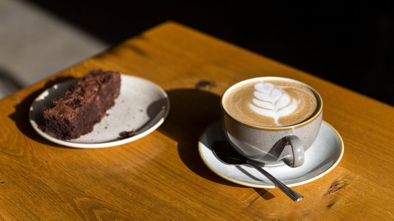 A piece of chocolate cake and a cup of coffee on a sunlit table